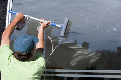 Professional window cleaner using a squeegee on a bright day